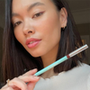 Eine Frau mit glattem, dunklem Haar trägt den SWEED Satin Eyeliner in Mintgrün auf, wodurch ihr natürliches Make-up und der Winged-Look besonders gut zur Geltung kommen.
