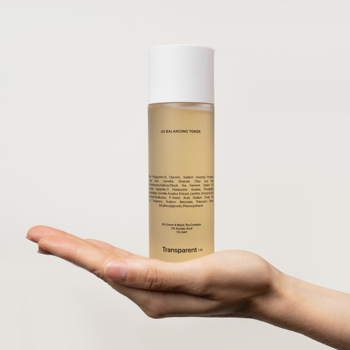 Eine Hand hält die A5 Balancing Toner Flasche von Transparent Lab vor einem schlichten, hellen Hintergrund.