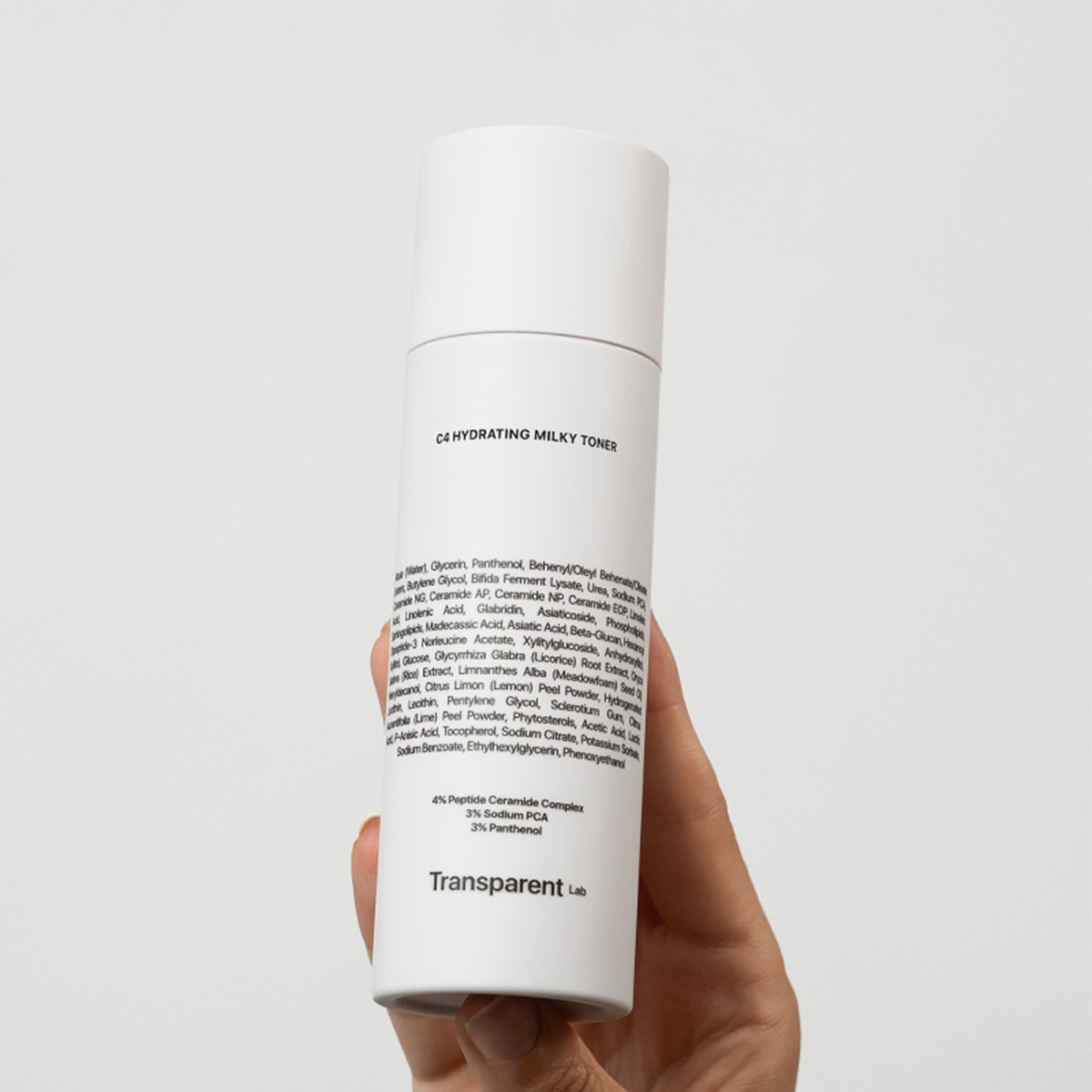 Eine Hand hält die Flasche des C4 Hydrating Milky Toner von Transparent Lab vor einem schlichten Hintergrund.