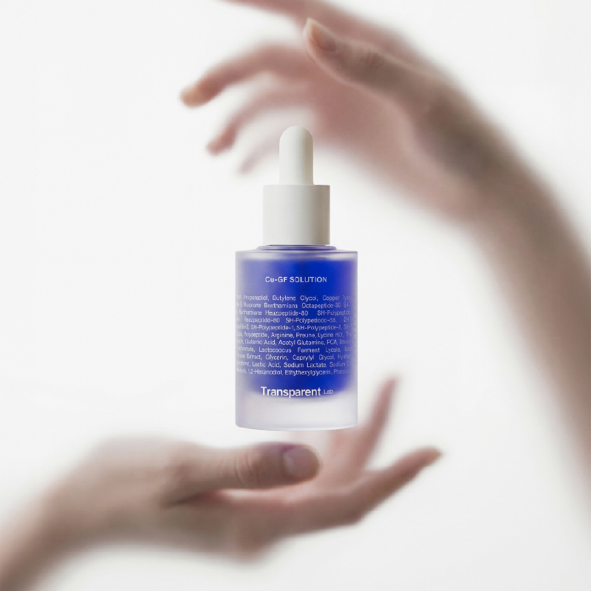Eine blaue Tropfflasche mit der Aufschrift Cu-Gf Solution von Transparent Lab wird zwischen zwei sanft verschwommenen Händen vor einem weißen Hintergrund gehalten.