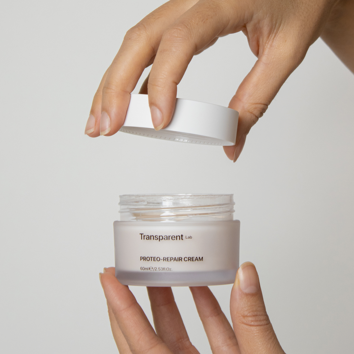 Eine Hand öffnet den Tiegel der Proteo-Repair Cream von Transparent Lab vor einem schlichten, hellen Hintergrund.