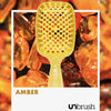 Eine gelbe UNbrush Detangling Hair Brush namens Amber auf einem Hintergrund aus polierten Bernsteinen.