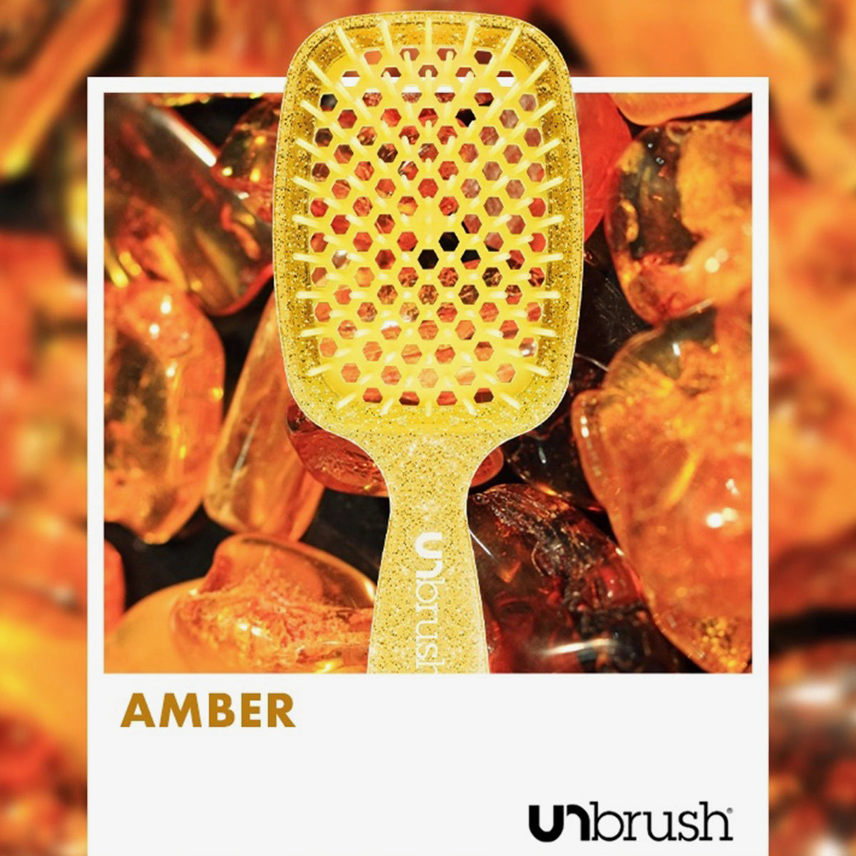 Eine gelbe UNbrush Detangling Hair Brush namens Amber auf einem Hintergrund aus polierten Bernsteinen.