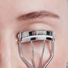Eine Nahaufnahme zeigt, wie die XLASH Cult Classic Wimpernzange an den oberen Wimpern angewendet wird.