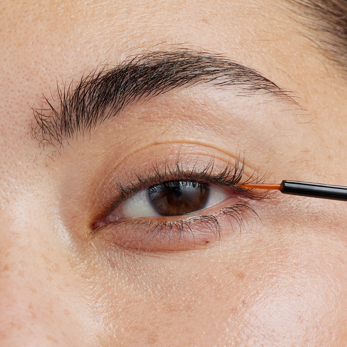 Eine Nahaufnahme einer Person, die das XLASH Xlash Wimpernserum (1 ml) mit einem dünnen Pinsel auf den oberen Wimpernkranz aufträgt.