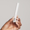 Eine Hand hält eine weiße Tube des Xlash Eyelash Serum vor einem schlichten, hellen Hintergrund.