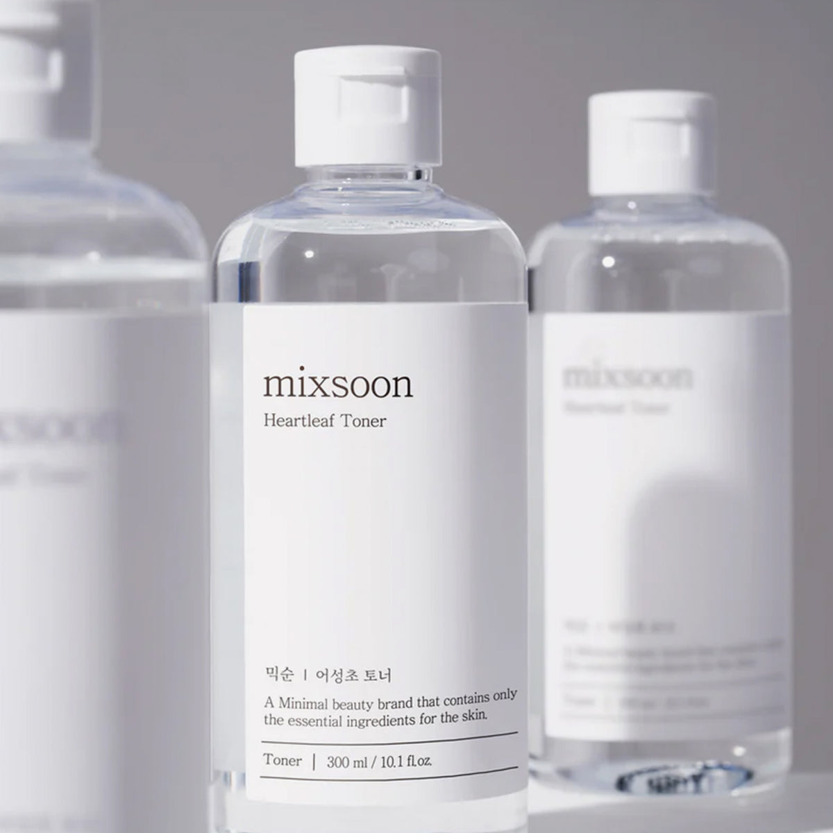Drei transparente Flaschen des Mixsoon Heartleaf Toners mit weißem Etikett, zentriert im Fokus, vor neutralem Hintergrund arrangiert.