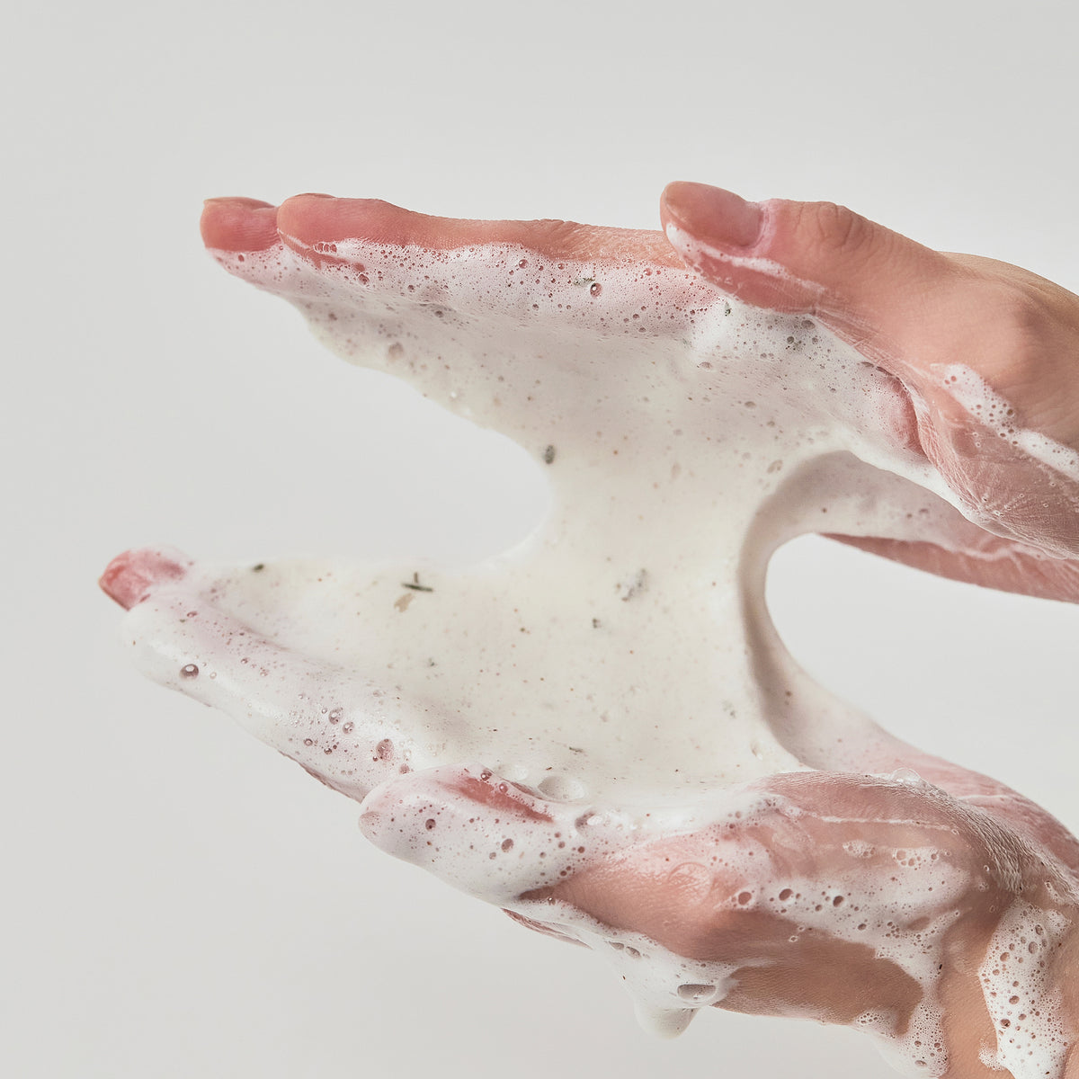 Hände halten und verteilen den weißen, schaumigen Schaum von Heartleaf Quercetinol Pore Deep Cleansing Foam vor einem schlichten, hellen Hintergrund.