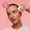 Frau, die Bali Body Face Tan Milk Drops aus einer weißen Flasche auf ihre Wange aufträgt.