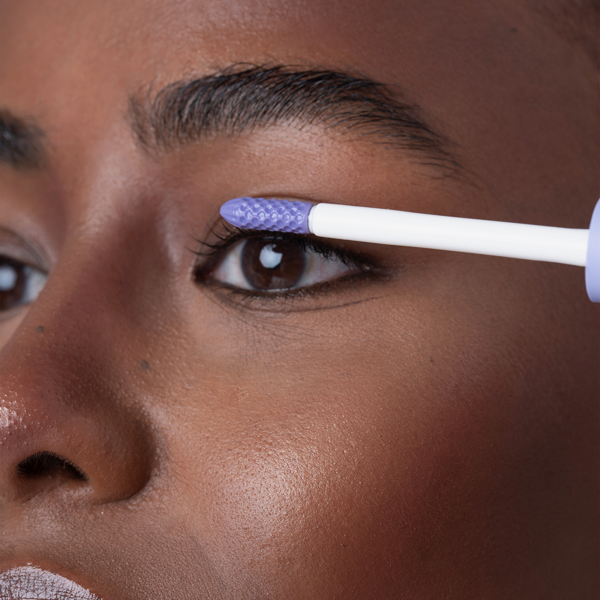 Jemand trägt das „BLONDESISTER 2 IN 1 EYES FIRST LASH&BROW SERUM“ mit einem weiß-blauen Applikator auf die oberen Wimpern auf.