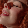 Eine Frau mit lockigem Haar und einem sanften Lächeln trägt „2 IN 1 IT’S UP TO YOU LIP OR CHEEK“ von BLONDESISTER und strahlt im warmen Sonnenlicht.