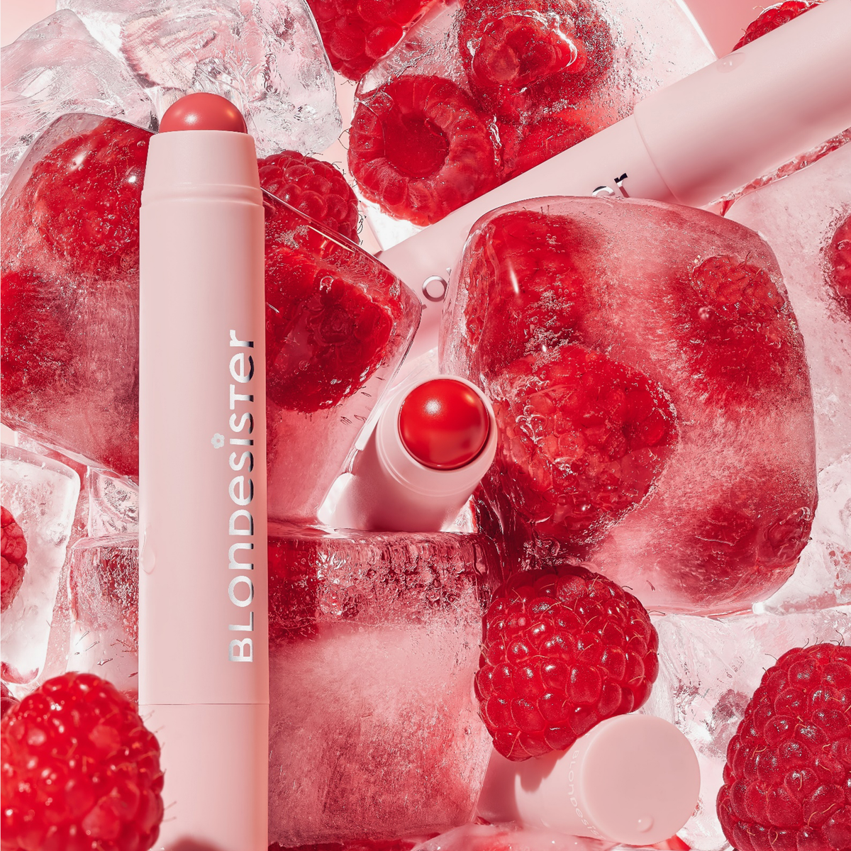 BLONDESISTER 2 IN 1 – DU HAST DIE WAHL: LIPPEN ODER WANGEN – mit Eiswürfeln und frischen Himbeeren vor einem rosa Hintergrund.