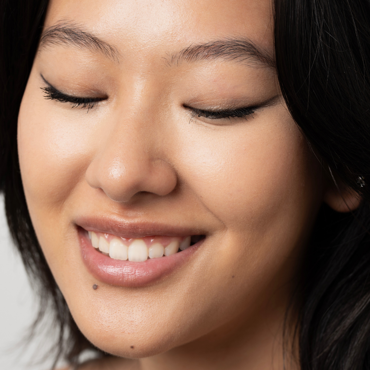 Eine Frau mit langen schwarzen Haaren und glatter Haut lächelt sanft, während sie den Lidschatten, den Eyeliner und den Kajal „BLONDESISTER 3 IN 1 EYES ON ME“ trägt.