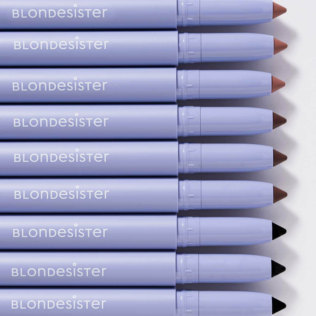 Acht „BLONDESISTER 3 IN 1 EYES ON ME“-Stifte in den Farbtönen Nude, Braun und Schwarz sind in einer Reihe angeordnet, sodass ihre farbigen Spitzen zu sehen sind.