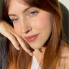 Eine Frau mit langen rotbraunen Haaren lächelt sanft und präsentiert die BLONDESISTER 4 IN 1 CLICK & TURN MASCARA im strahlenden Sonnenlicht.