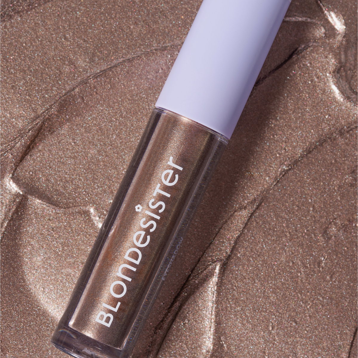 Ein GLOWEYE-LIDSCHATTEN von BLONDESISTER liegt auf einer strukturierten, schimmernden bronzefarbenen Oberfläche.