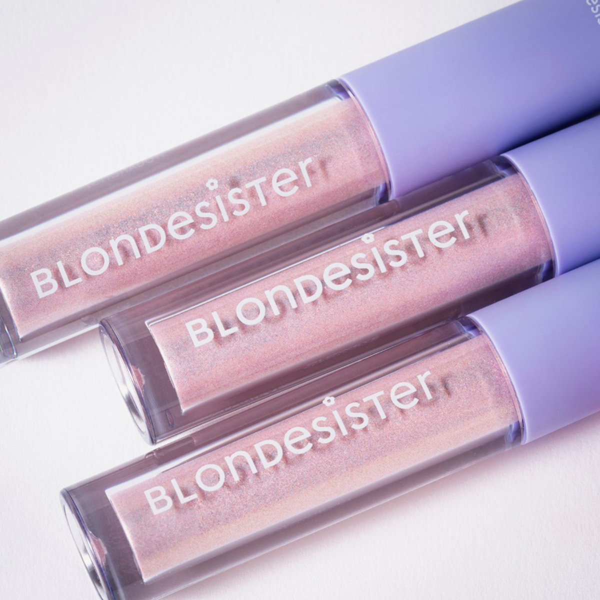 Drei GLOWEYE-Lidschatten-Tuben von BLONDESISTER mit lavendelfarbenen Verschlusskappen sind diagonal auf einer weißen Fläche angeordnet.