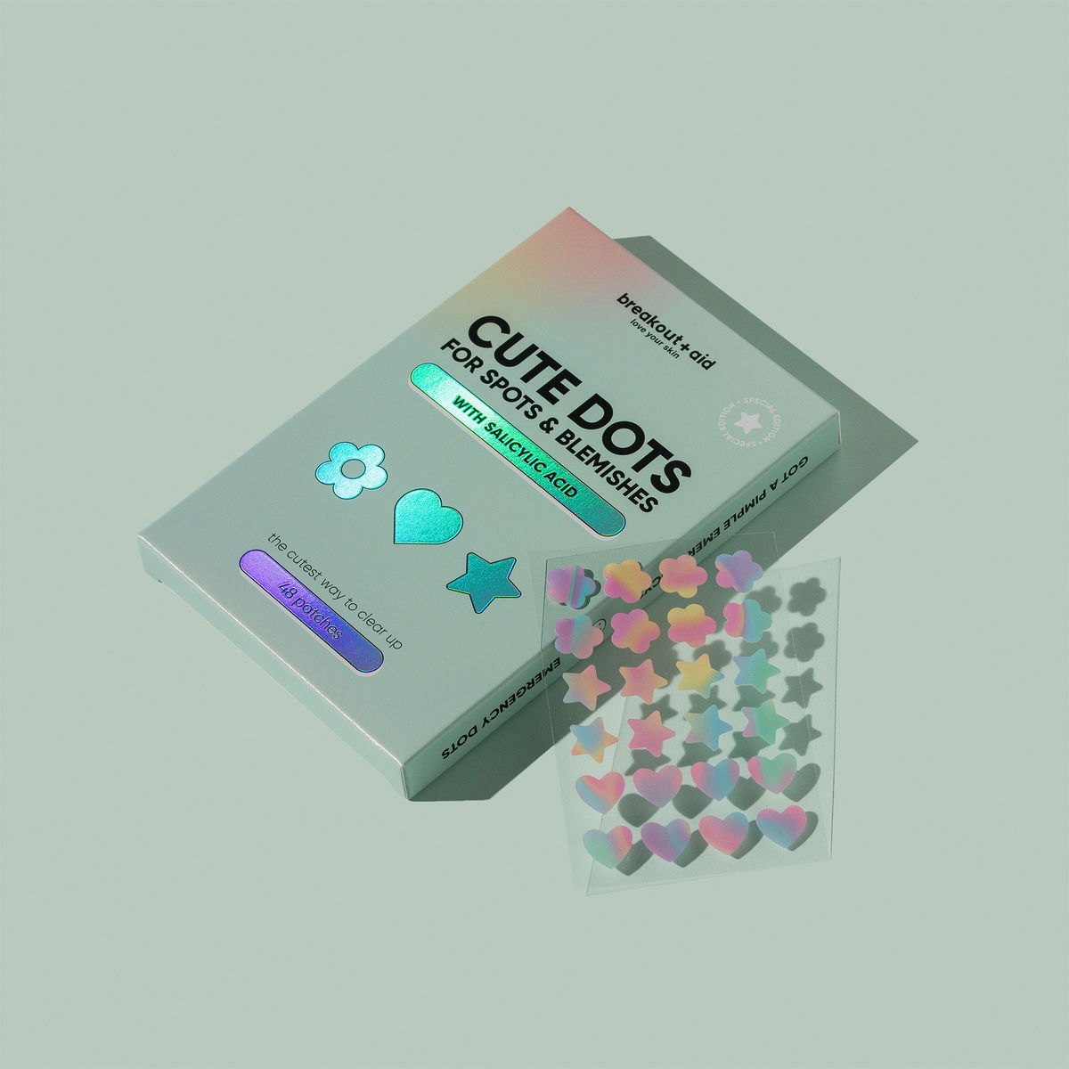 Eine Packung Cute Dots for Spots & Blemishes-Akne-Pflaster mit einem Bogen holografischer Aufkleber in Form von Blumen, Herzen und Sternen.