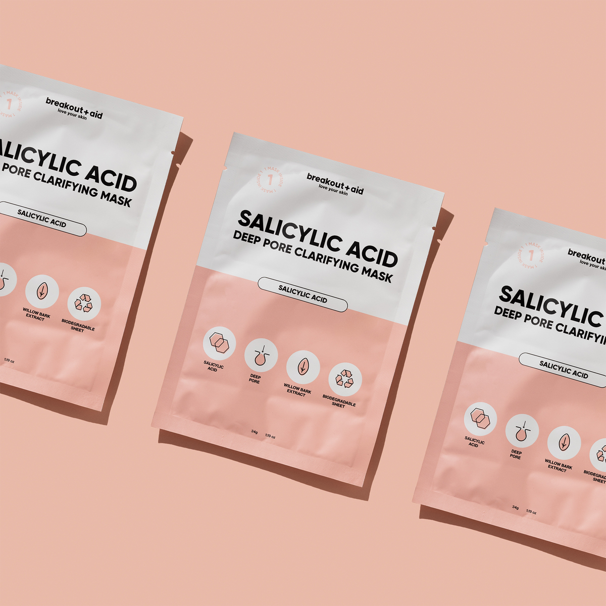 Drei weiße und hellrosa Beutel mit der Breakout+Aid Salicylic Acid Clarifying Mask, diagonal auf einem hellrosa Hintergrund angeordnet.