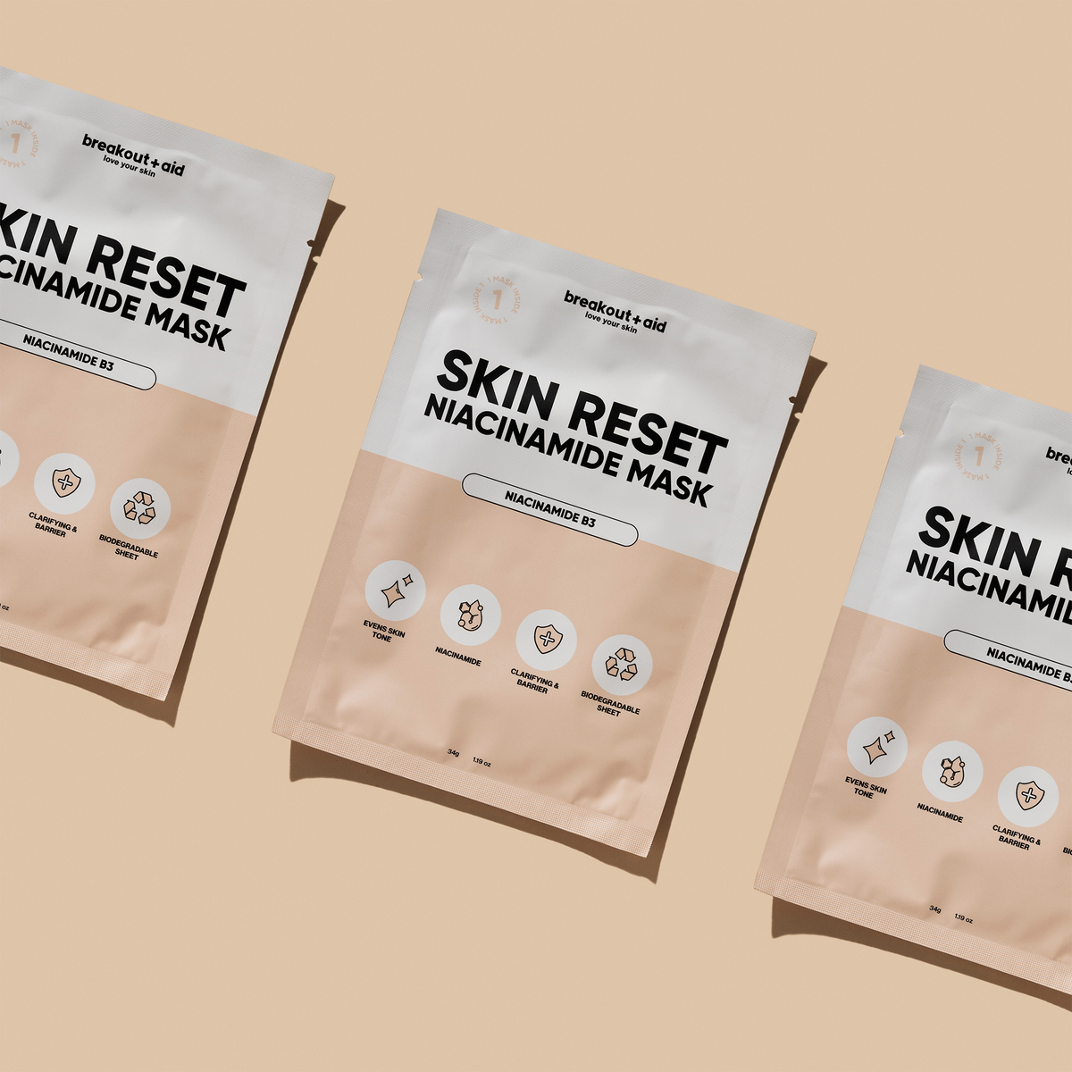 Drei rechteckige Breakout+Aid Skin Reset Niacinamide Mask-Päckchen, die diagonal auf einem hellbraunen Untergrund angeordnet sind.