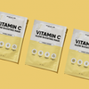 Drei gelbe Päckchen mit der Breakout+Aid Vitamin C-Maske, angeordnet auf einem gelben Hintergrund.
