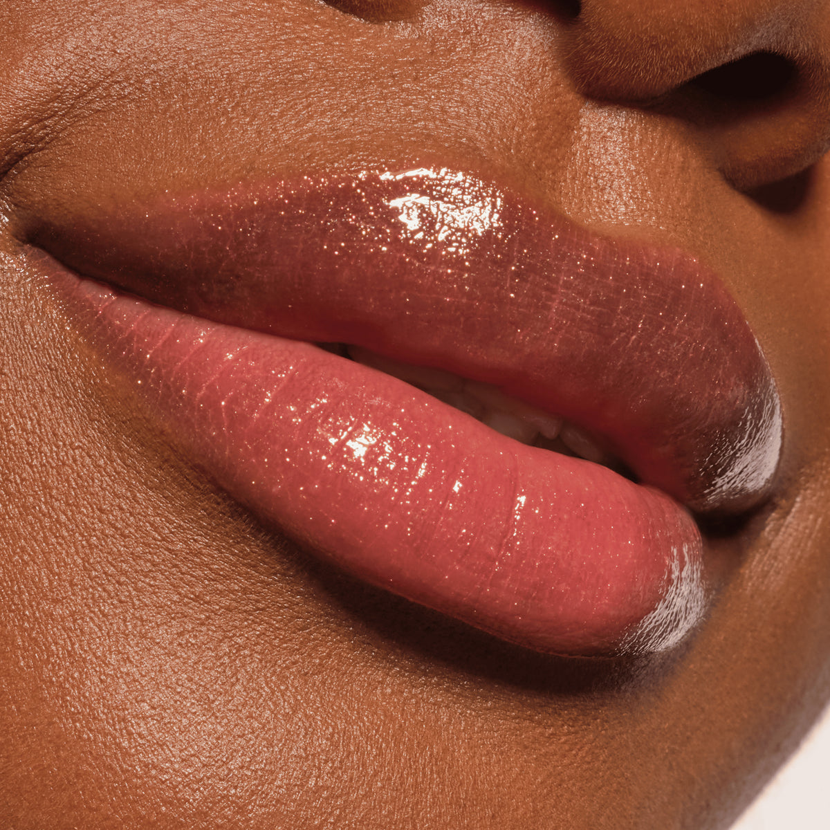Nahaufnahme von glänzenden rosa Lippen auf dunkler Haut, die den Glanz und die glatte Textur des Diamond Glaze Gloss Stick hervorheben.