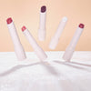 Fünf schimmernde Catrice Diamond Glaze Gloss Sticks in verschiedenen Farben, scheinbar schwebend, vor einem warmen Hintergrund auf glitzernder Fläche.