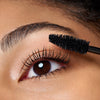 Nahaufnahme eines Auges, während Catrice Cosmetics Hyper Lash Mascara 010 mit einem schwarzen Mascarastift auf die oberen Wimpern aufgetragen wird.