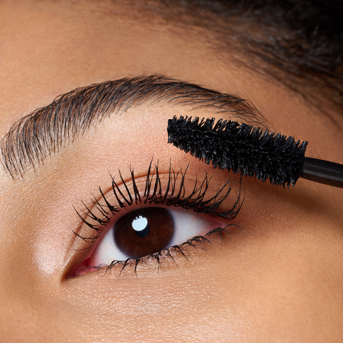 Nahaufnahme eines Auges, während Catrice Cosmetics Hyper Lash Mascara 010 mit einem schwarzen Mascarastift auf die oberen Wimpern aufgetragen wird.