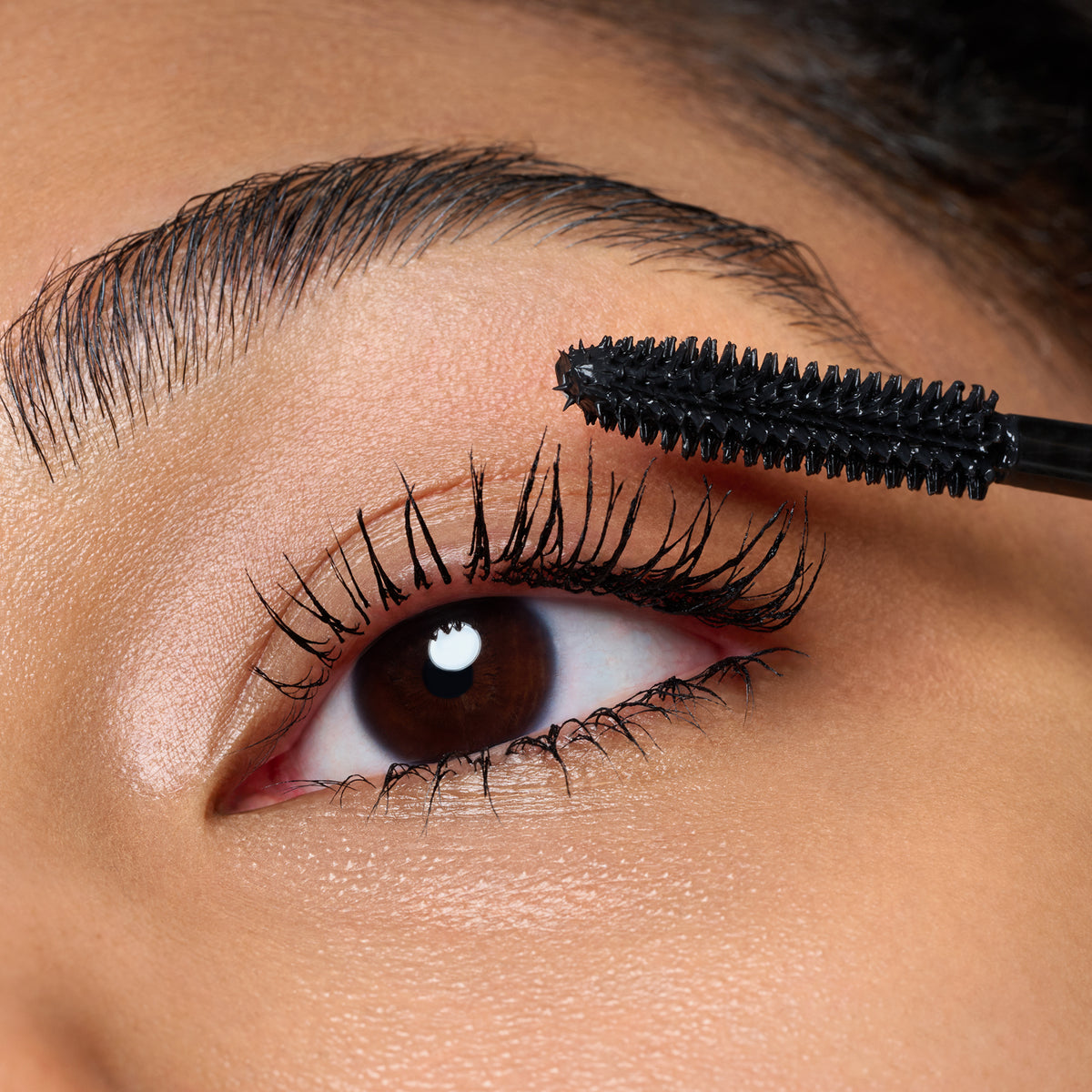 Nahaufnahme einer Person, die Catrice Cosmetics TUBING Stay In Place Volume Mascara 010 auf ihre oberen Wimpern aufträgt.