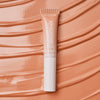 Eine Tube Catrice Cosmetics Under Eye Brightener Liquid auf einem strukturierten pfirsichfarbenen Hintergrund.
