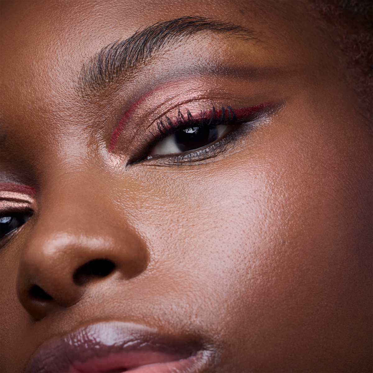 Nahaufnahme einer schwarzen Person mit leuchtendem, schimmerndem Augen-Make-up in Rosa- und Rottönen.