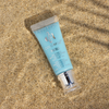 Eine Tube Danessa Myricks Beauty Colorfix Pastels Oasis liegt auf dem Sandstrand und leuchtet im Sonnenlicht.