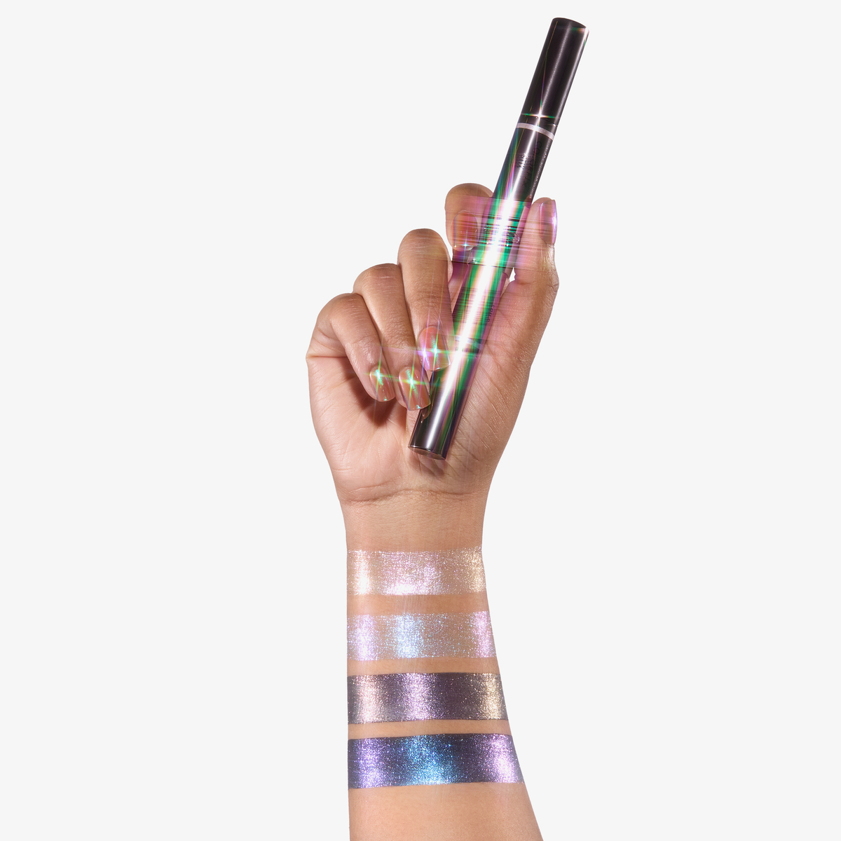 Eine Hand hält Danessa Myricks Beauty Colorfix Stix Infinity; auf dem Unterarm befinden sich schimmernde Lidschattenproben in verschiedenen Farben.