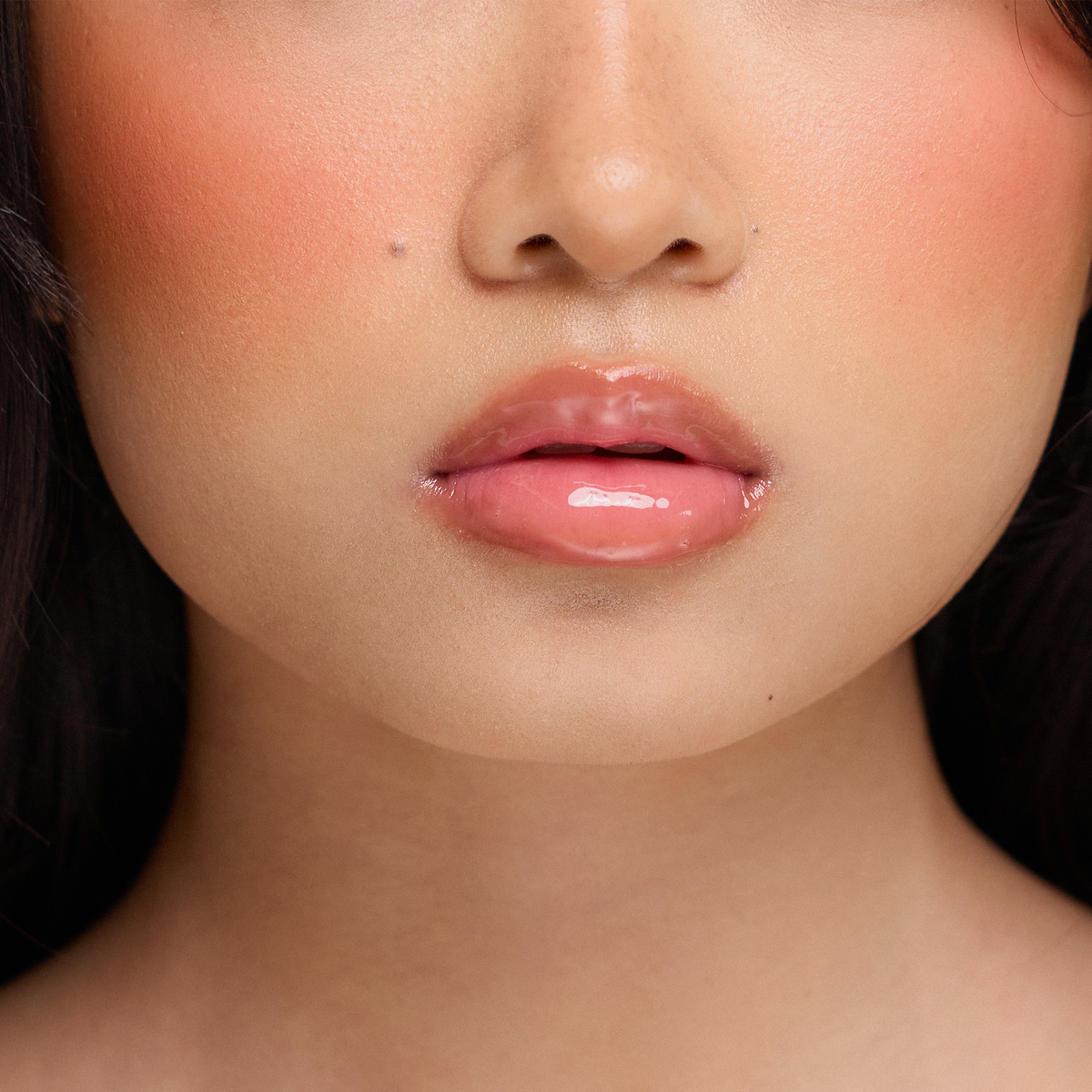 Nahaufnahme von glänzenden rosa Lippen mit Dominique Cosmetics Juicy Lip Balm, glatter Haut und pfirsichfarbenem Rouge auf den Wangen.