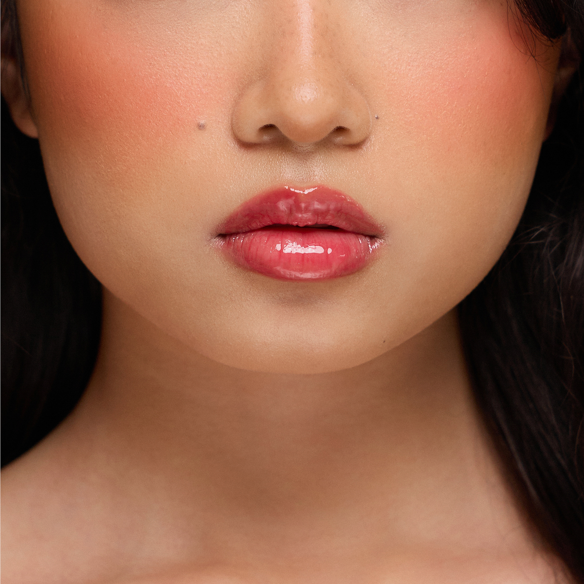 Nahaufnahme einer Frau, die Dominique Cosmetics Juicy Lip Balm in einem glänzenden rosa-roten und pfirsichfarbenen Make-up trägt.