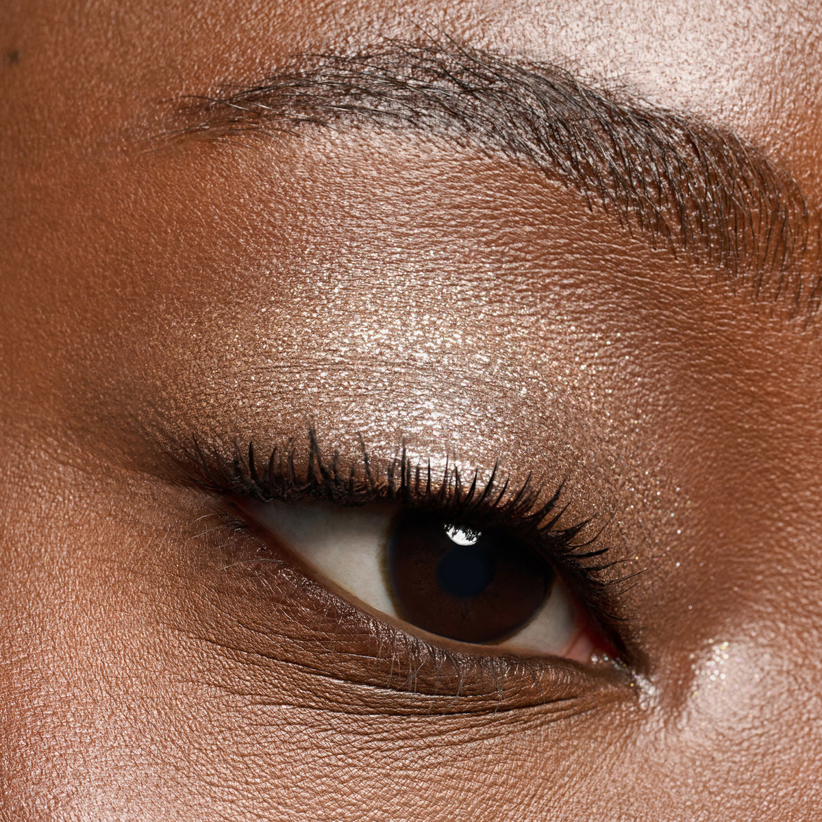 Nahaufnahme eines braunen Auges, das mit dem Essence JELLY JEWELS Glitter Stick verziert wurde, mit schimmerndem Goldlidschatten und definierten Wimpern.