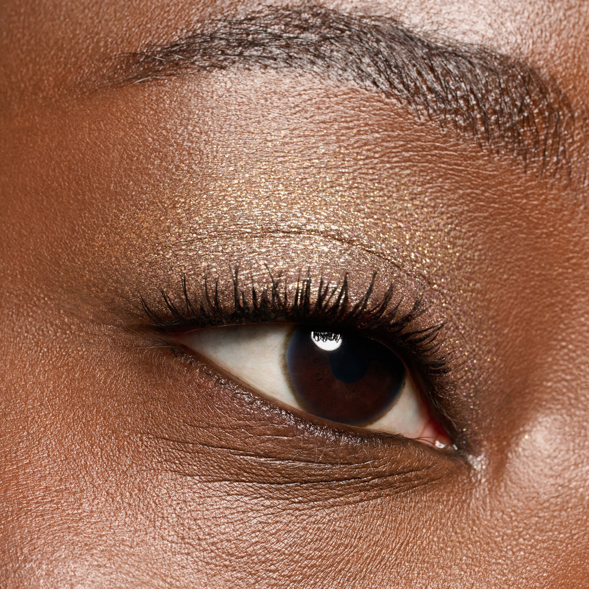 Nahaufnahme eines Auges mit golden schimmerndem Lidschatten, langen Wimpern und gut definiertem Augenbrauenbogen.