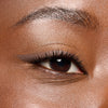 Nahaufnahme eines braunen Auges mit sanftem braunem Eyeliner und langen, geschwungenen Wimpern auf glatter Haut.