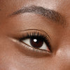 Nahaufnahme eines Auges mit brauner Iris und zartem goldschimmerndem Eyeliner am unteren Lidrand, dezentes Make-up auf warmer Haut.