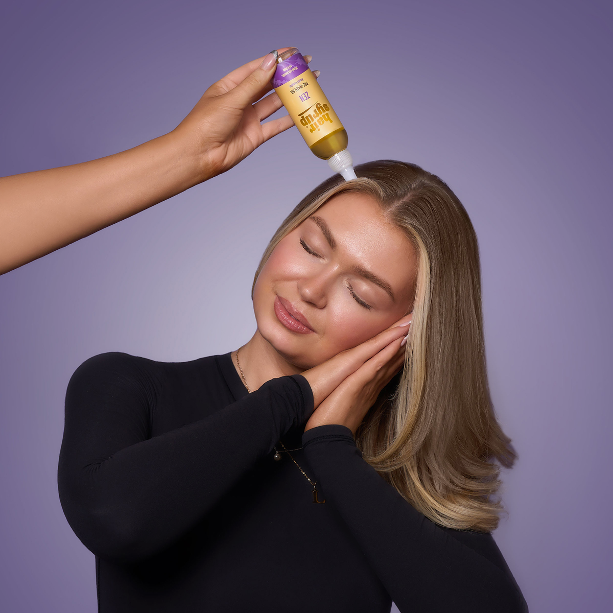 Eine Frau mit geschlossenen Augen trägt das Zen-Haaröl von Hair Syrup vor einem violetten Hintergrund auf ihre Kopfhaut auf.