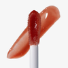 Eine Nahaufnahme des Applikators für den Lipgloss „Over The Garden Wall – Potatoes & Molasses Swirled“ von Lethal Cosmetics, im Hintergrund ein rotes Farbmuster.