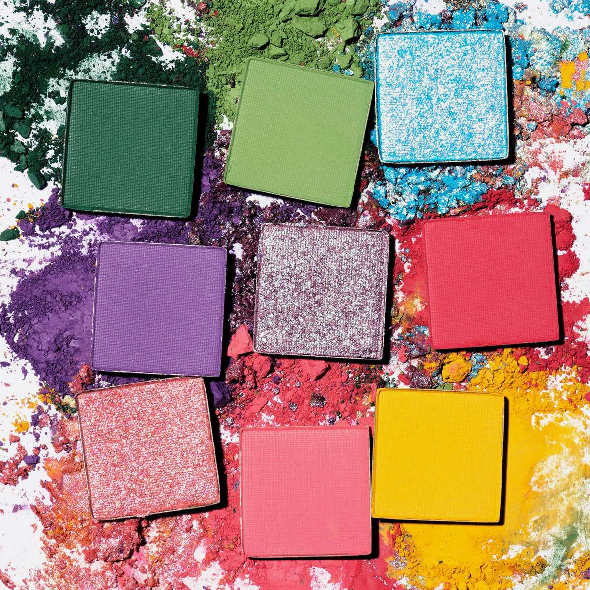 Neun farbenfrohe, teils glitzernde Puder aus der Palette 1993 von LH Cosmetics, verstreut auf einer weißen Fläche mit Puderspritzern.