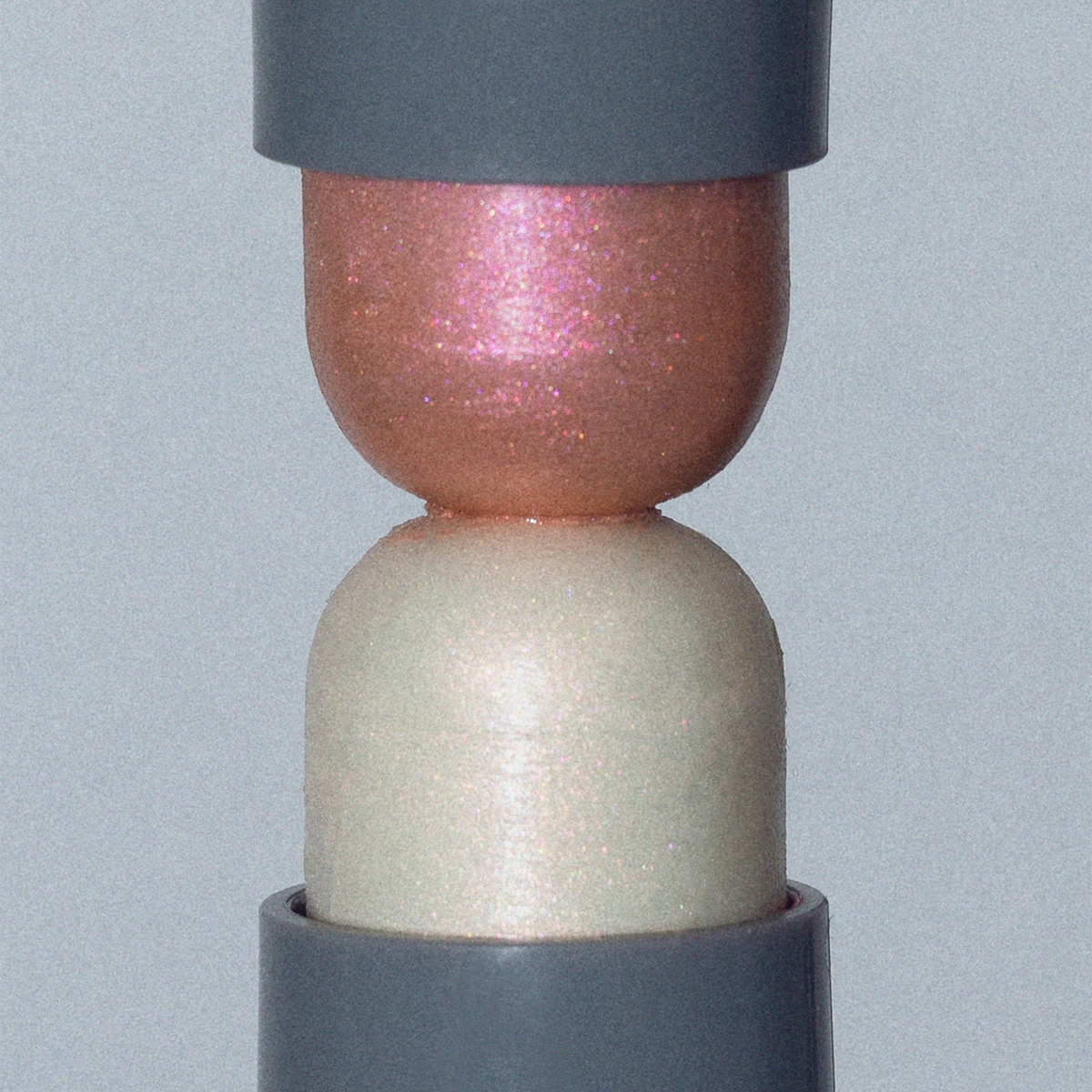 LH Cosmetics Artistick Highlighter: zwei kuppelförmige, schimmernde Balsame (rosa und weiß), die in grauen Halterungen stecken.