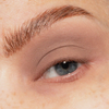 Eine Nahaufnahme eines blauen Auges mit natürlichem Make-up und einer hochgezogenen Augenbraue mit The Single von LH Cosmetics.
