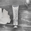 Eine Tube Marvis Zahnpasta Smokers Whitening Mint liegt auf einer grauen Fläche neben weißen Steinen und einem Glasobjekt.