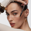 Frau mit Sommersprossen trägt den NABLA Cosmetics Freckle Maker Pen auf, trägt Goldschmuck und neutrales Make-up.