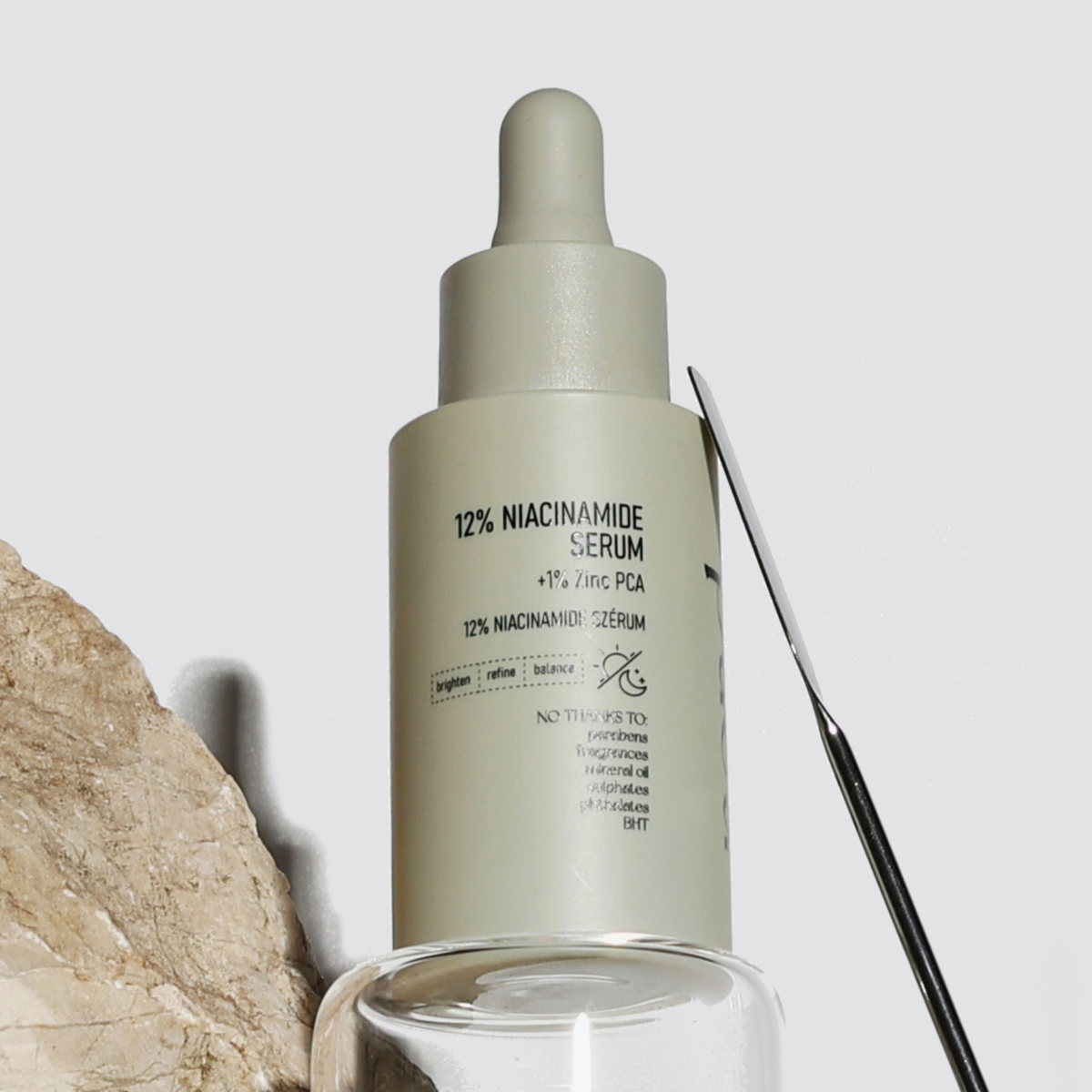 Eine Flasche NERDS. 12% Niacinamide + 1% Zinc PCA Serum mit einem Tropfer sitzt neben einem Stein und einem Glasbehälter.