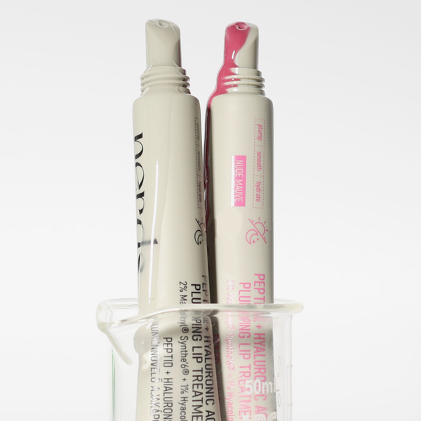 Zwei Tuben der NERDS. Peptide + Hyaluronic Acid Lip Treatment stehen in einem klaren Glasbecher.