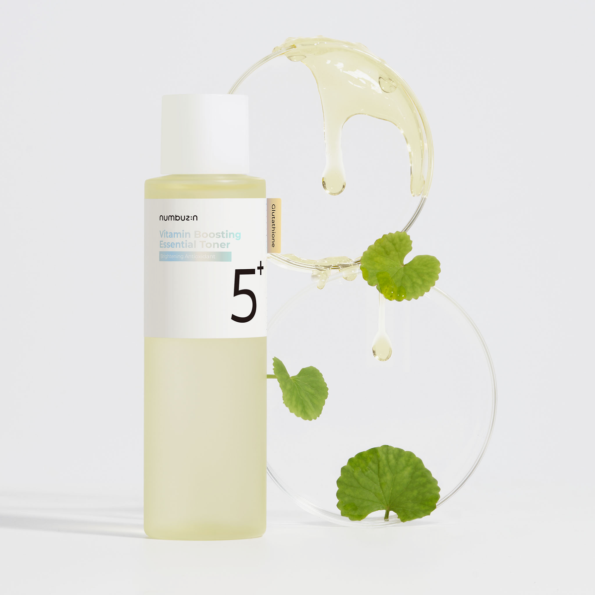 Gelber Numbuzin No.5 Vitamin Boosting Toner mit weißem Deckel, daneben Glasplatten mit grünem Blatt und tropfender Flüssigkeit.